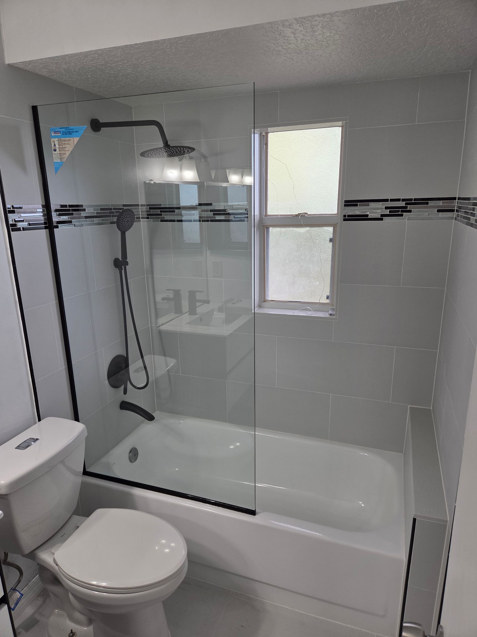 A modern bathroom with a shower, tub, and toilet. White tile, black accents, and a window.