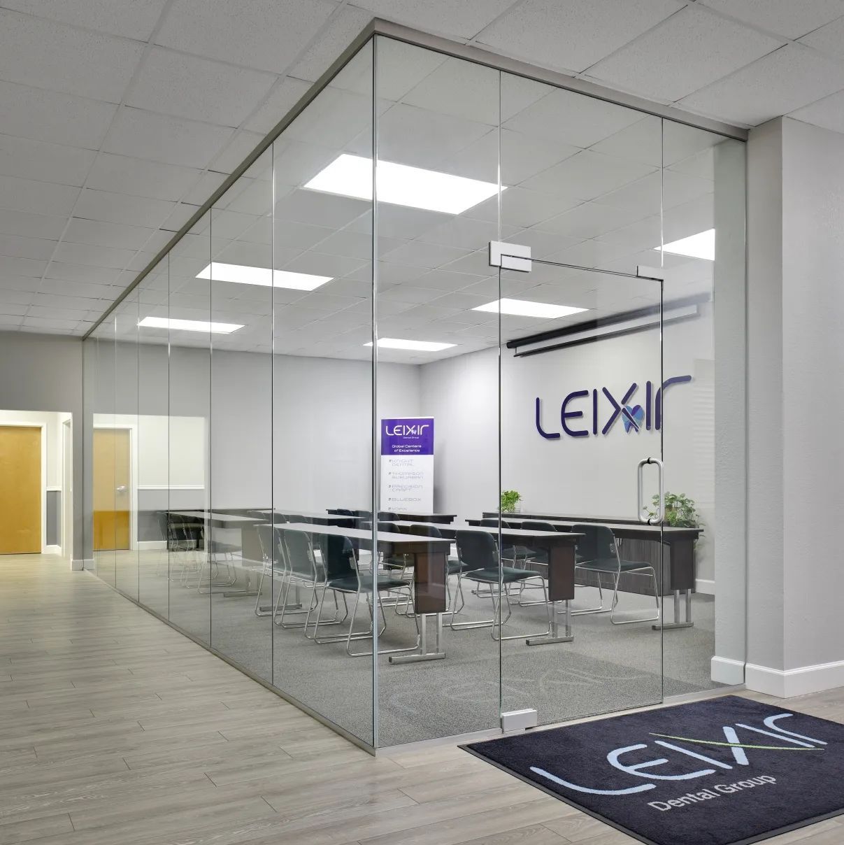 Glass-walled conference room with long table and chairs; hallway in foreground, company logo on the wall.