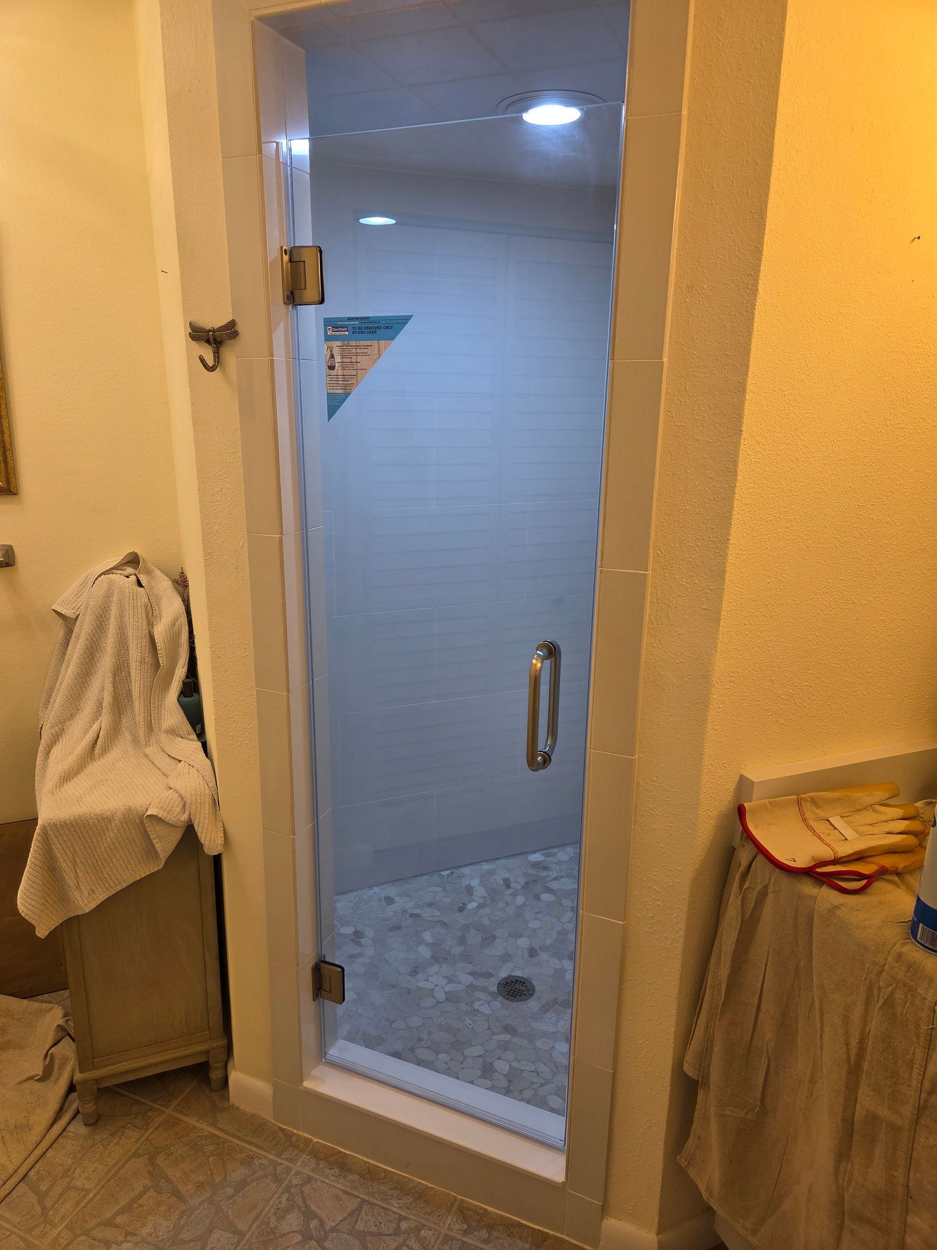 Glass shower door in a bathroom with white tile walls and a stone floor.