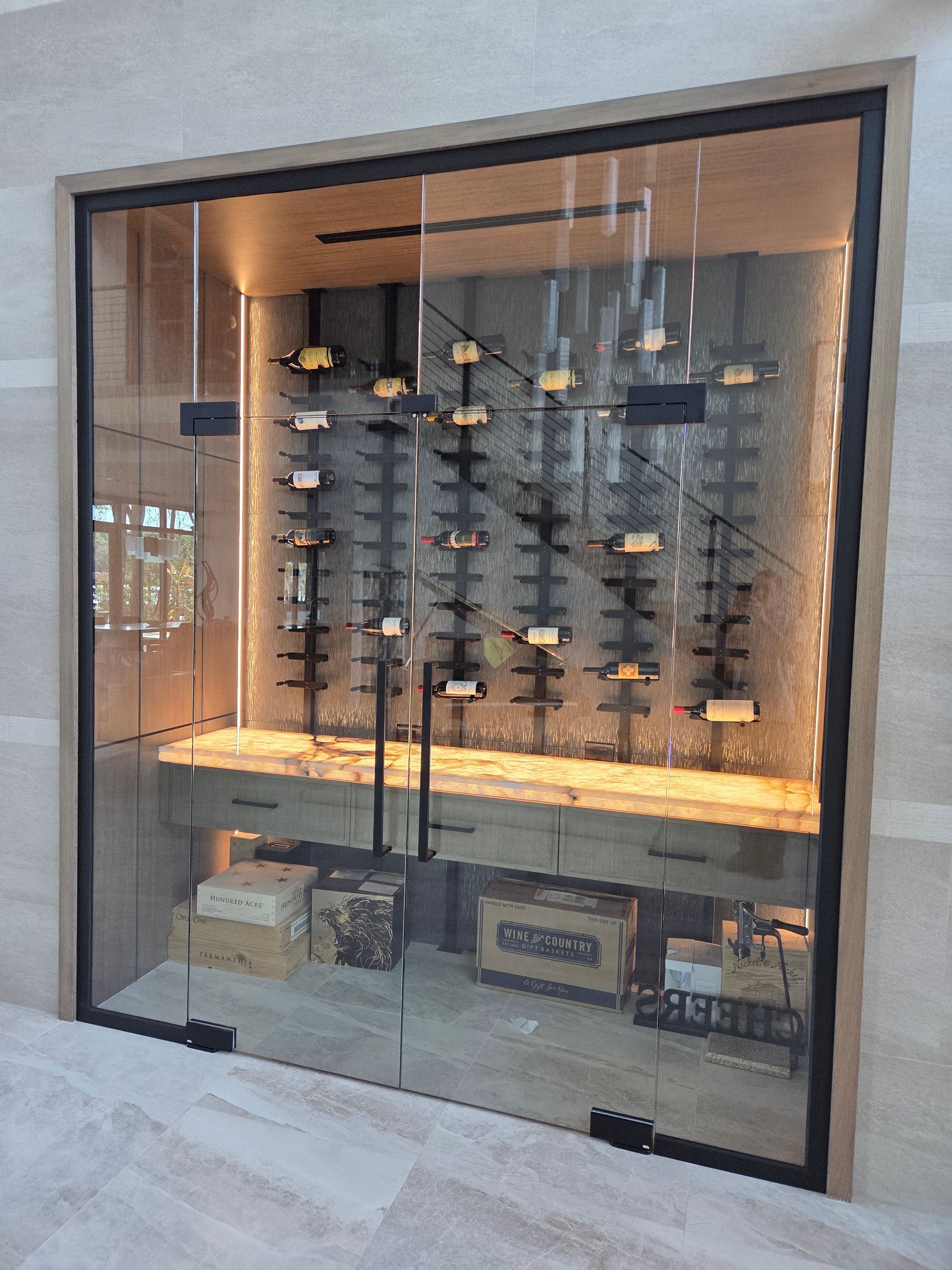 Glass-enclosed wine storage with multiple bottles on racks, wooden interior, and base storage area.