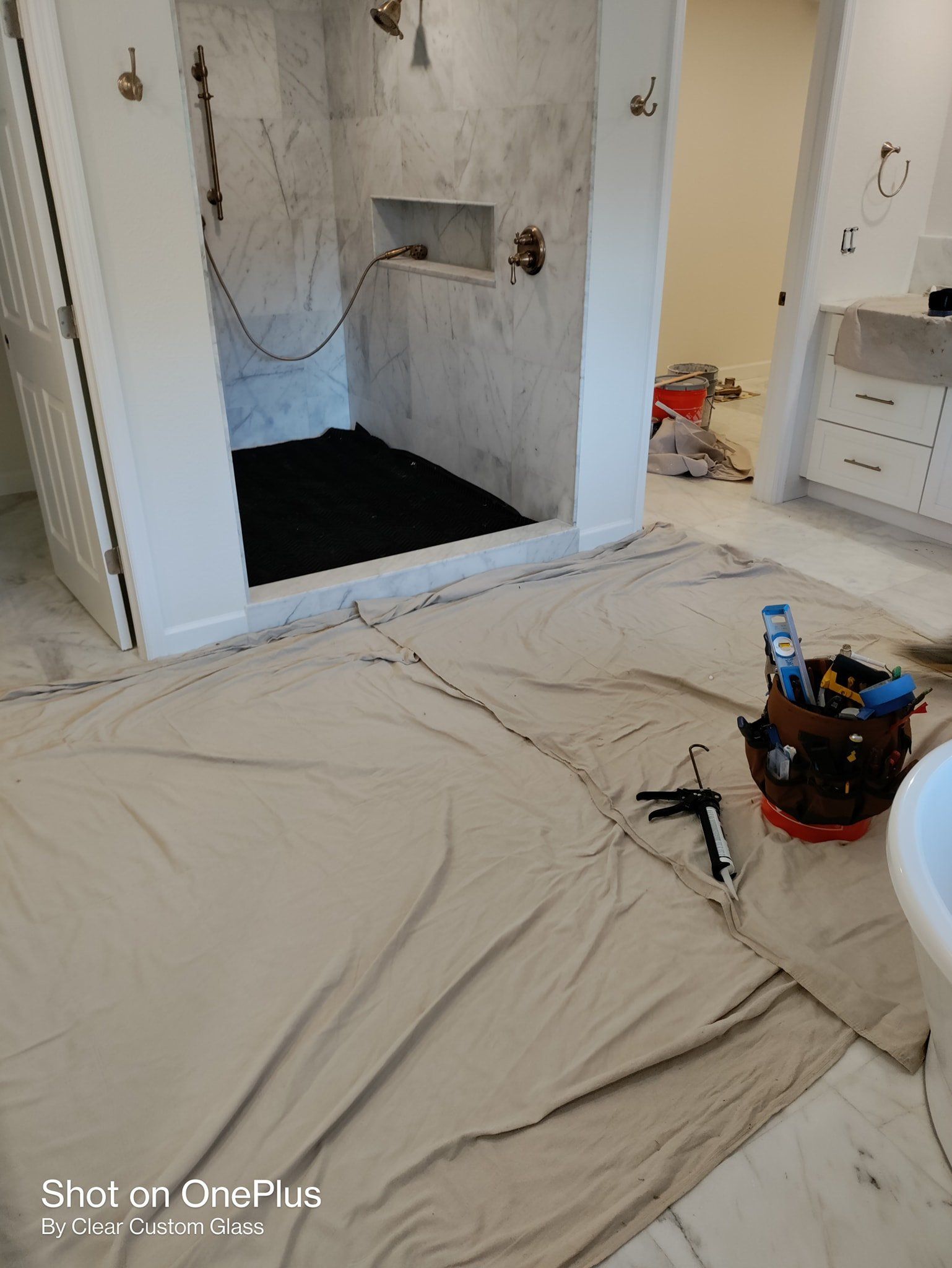 Bathroom undergoing renovation, shower stall with marble tile. Paint covers floor; tools and caulk present.