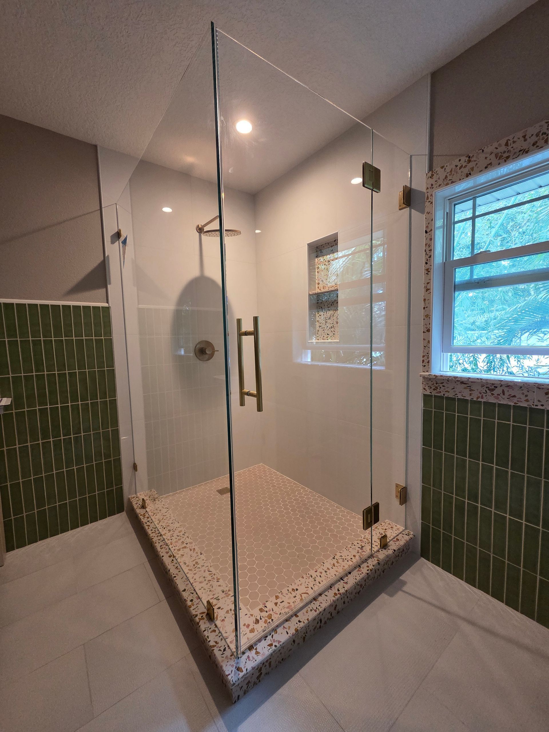 Modern bathroom with glass shower enclosure, green and white tile.