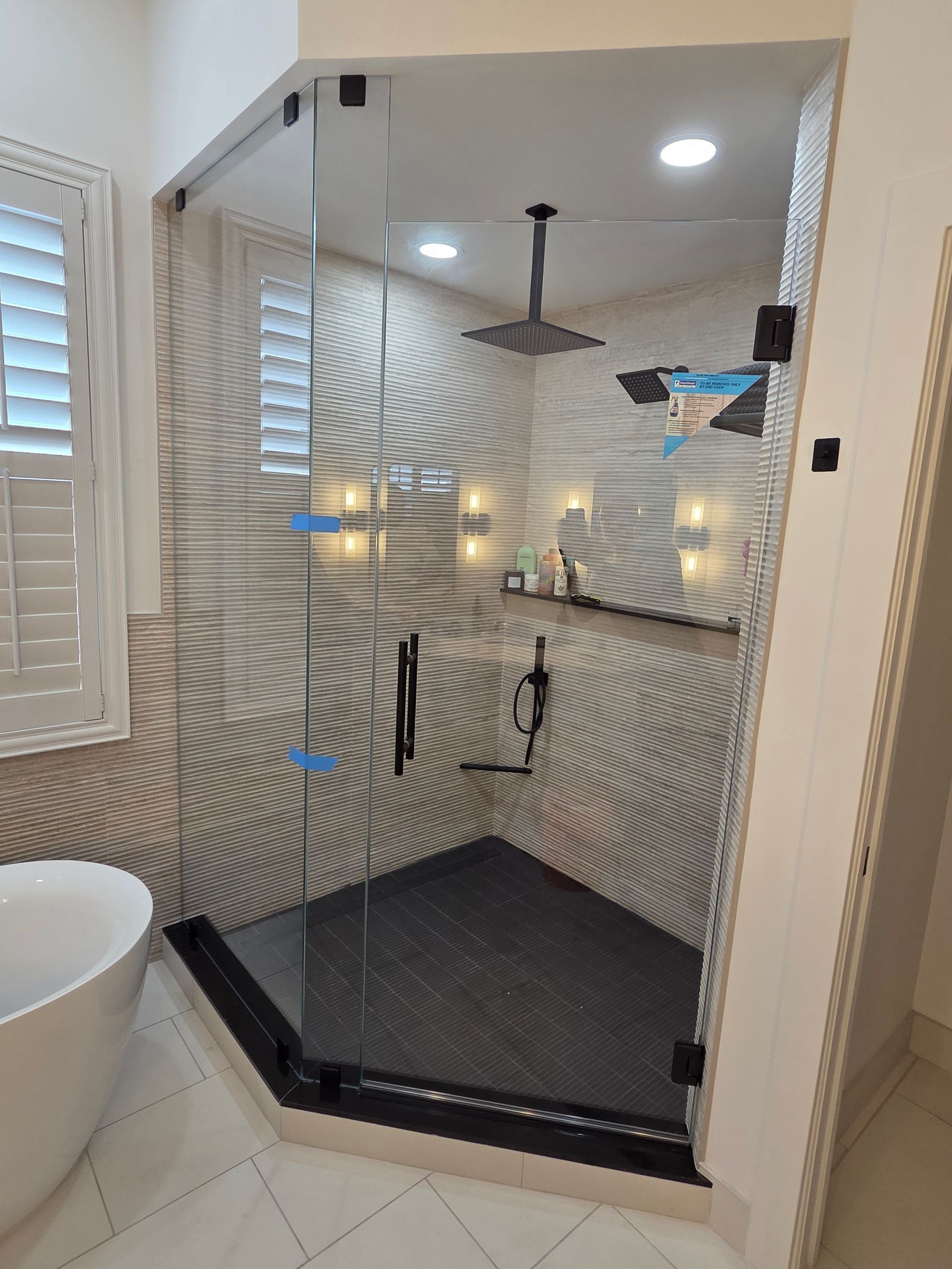 Modern walk-in shower with tiled walls, black hex floor, and glass entry in a bright bathroom