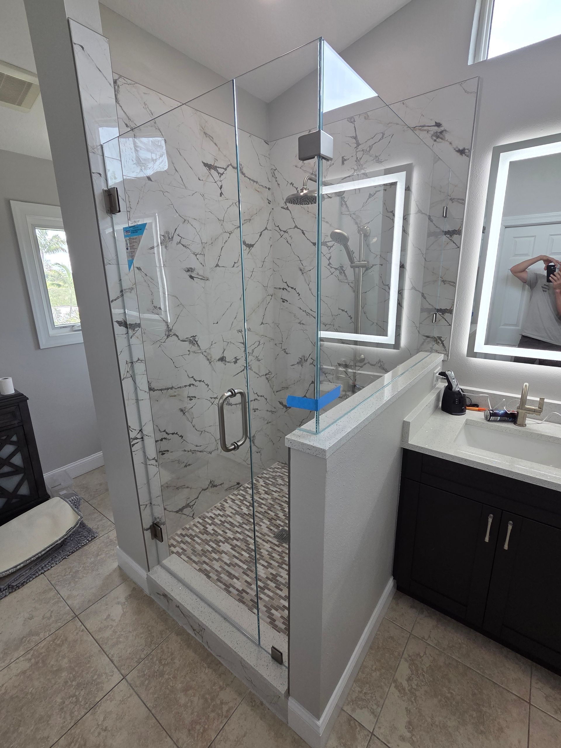 Modern bathroom with glass shower, white vanity, and toilet visible in the background