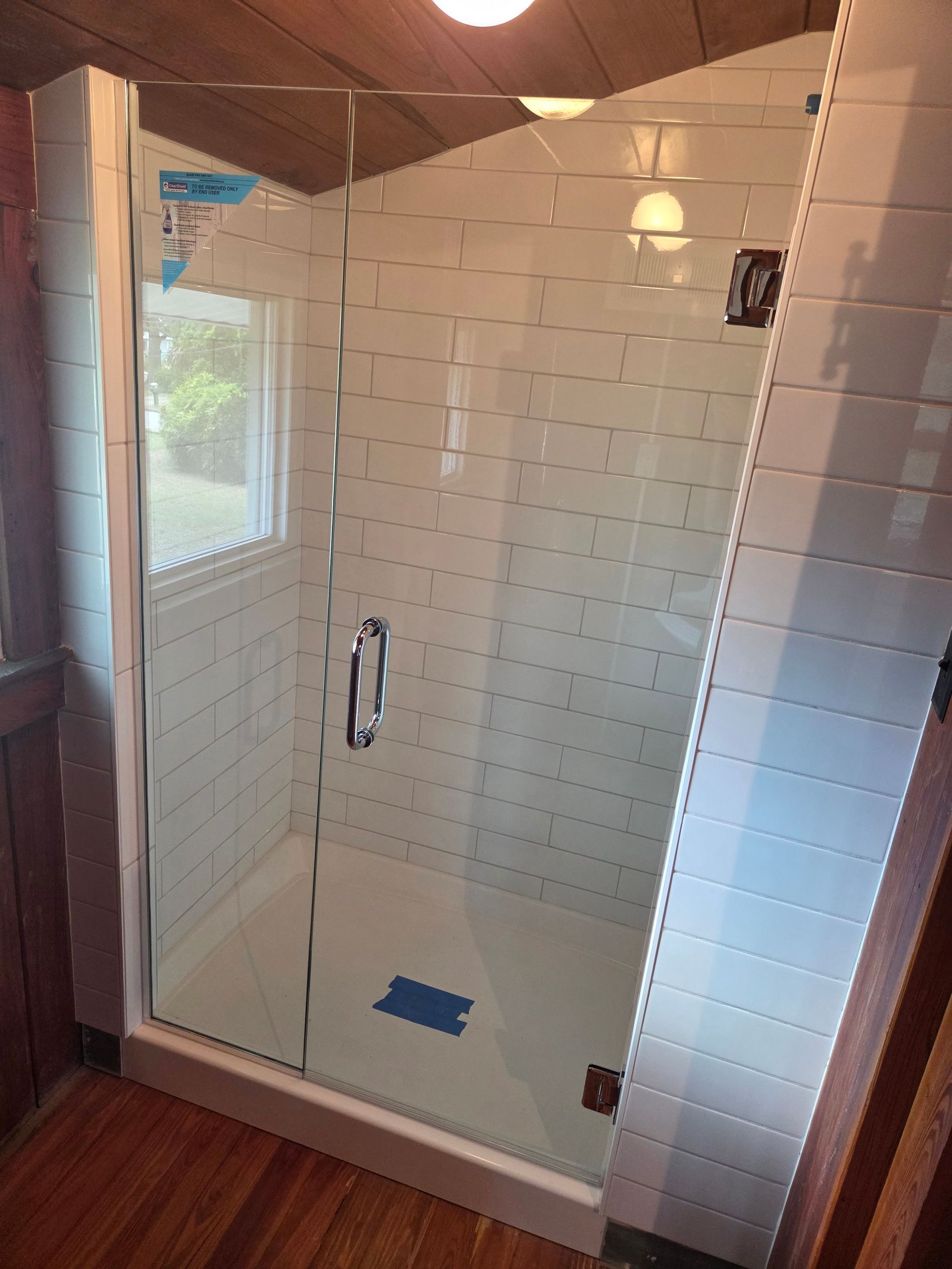 Modern tiled shower with glass door, white walls, bench, and a window