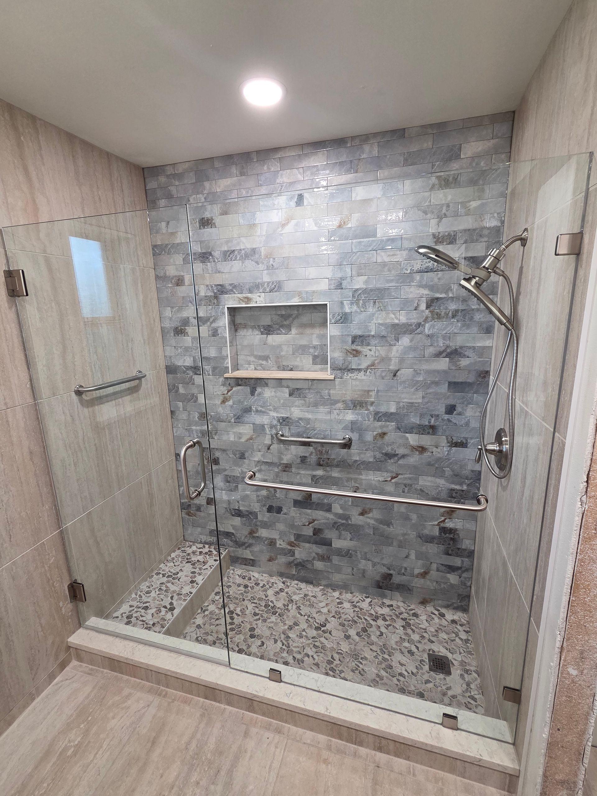 Walk-in shower with gray stone tile, built-in shelf, and glass door in a modern bathroom