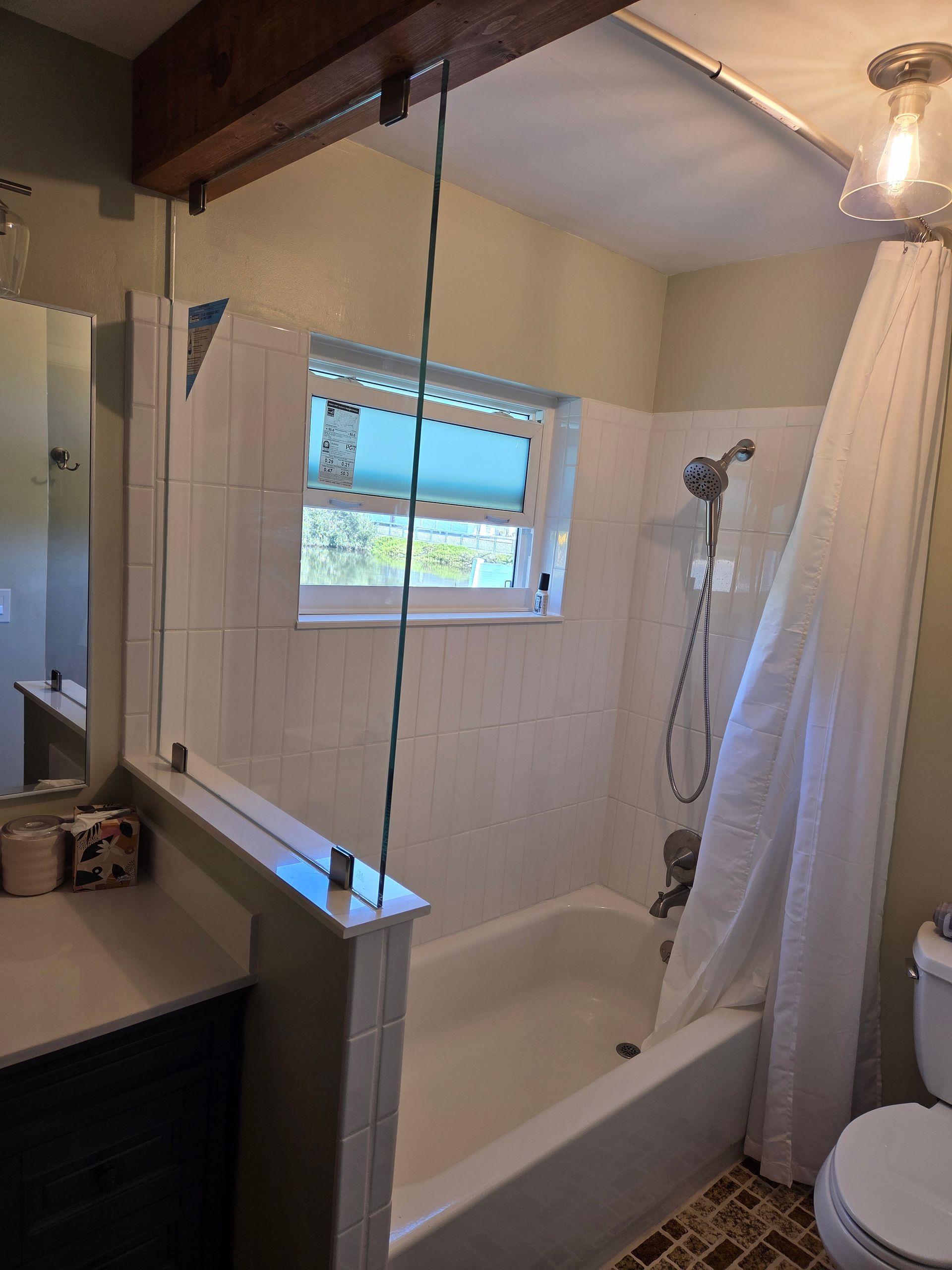 Bathroom with tub, showerhead, and white shower curtain. Light colored walls, a window above the tub, and a dark wood beam.