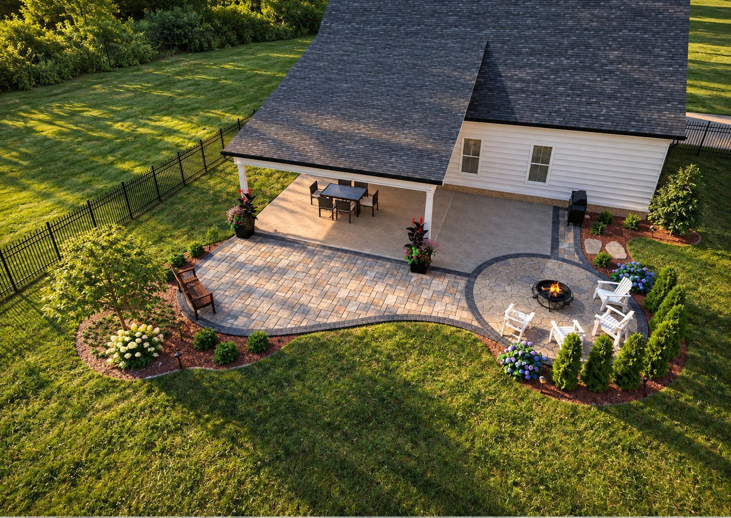 Aerial view of a house with a patio, outdoor seating, and a circular fire pit in a landscaped yard.