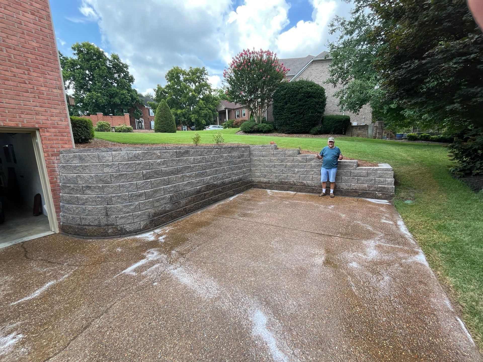 Concrete driveway beside stone retaining wall, with a child standing on the wall in a backyard.