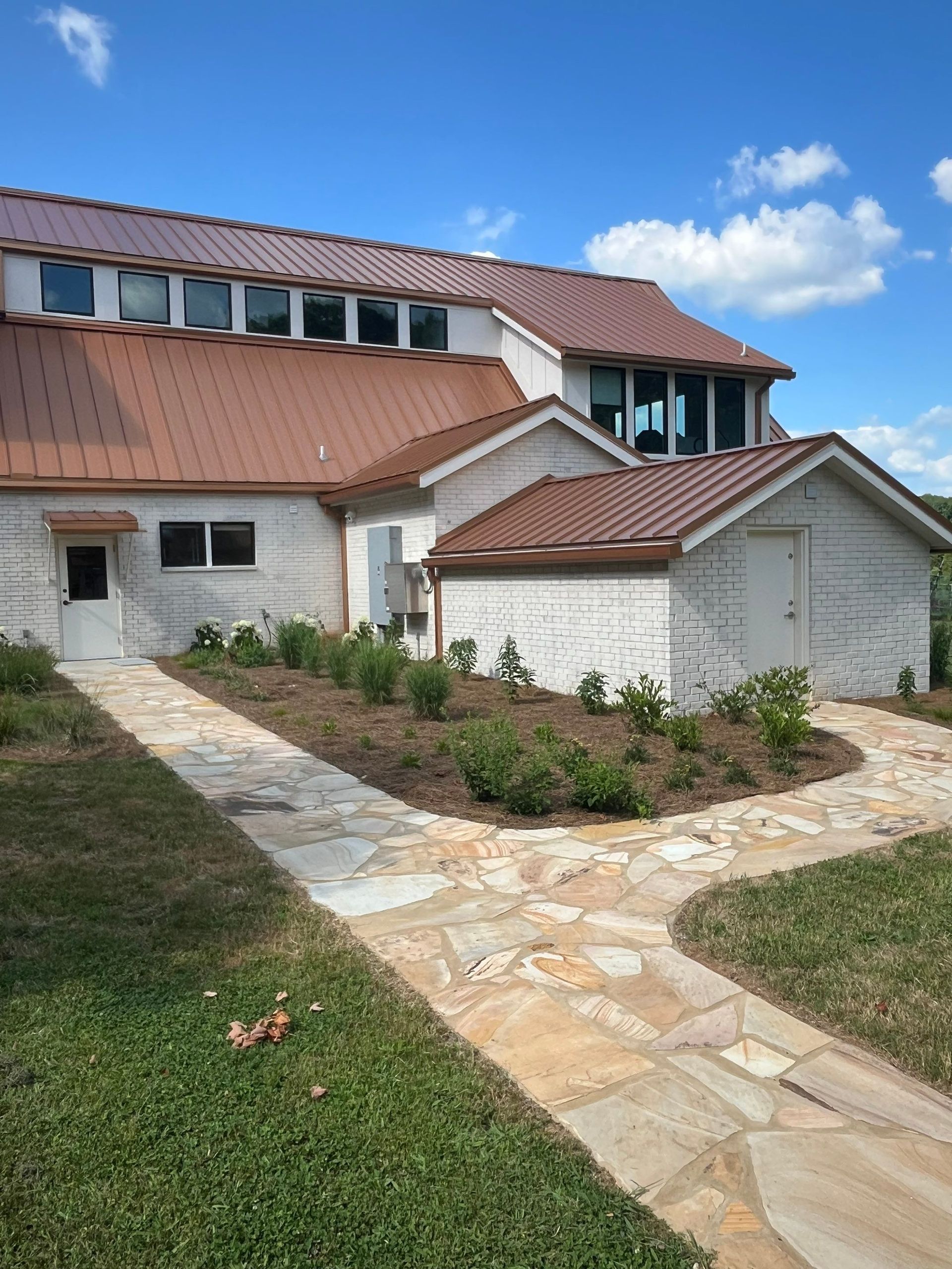 Stone walkway leading to a white building with a red tile roof and landscaped garden under a blue sky