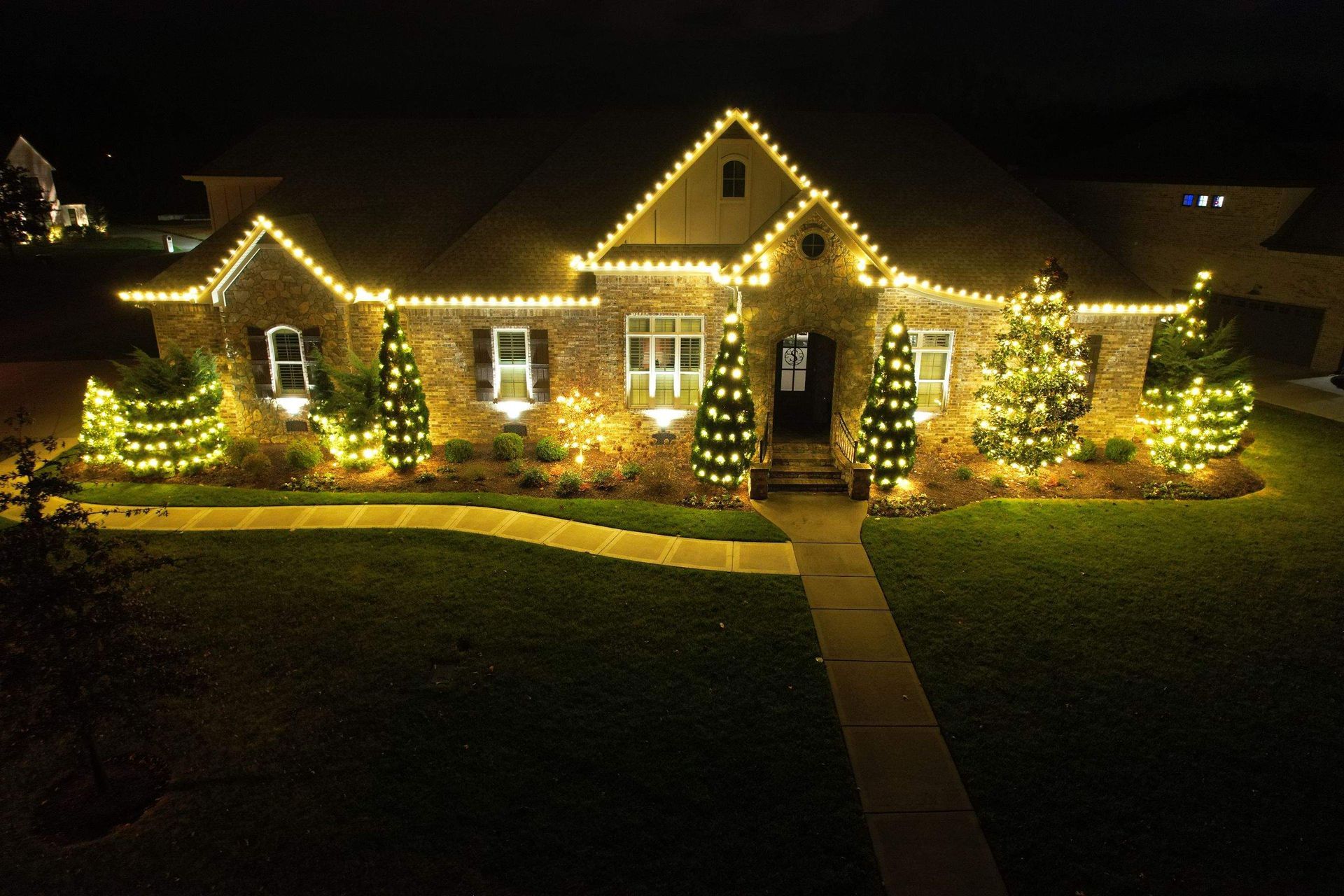 House decorated with warm white Christmas lights at night, with lit trees and a walkway in front