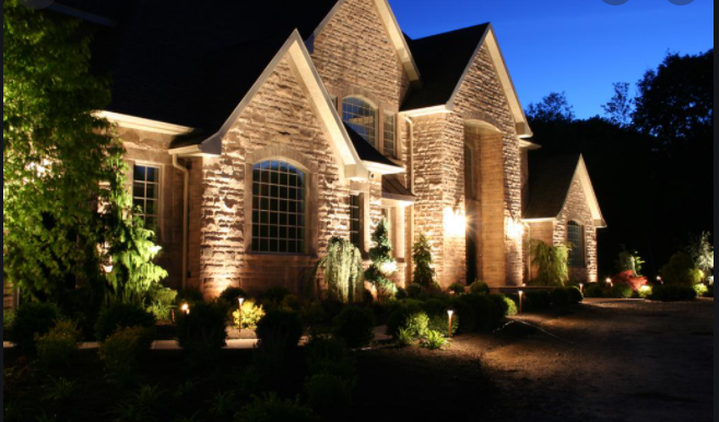 Stone house illuminated at night with landscaped yard.