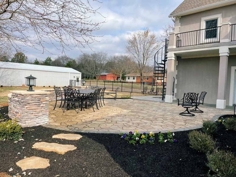Patio with black furniture, spiral staircase, and landscaping next to a two-story building.