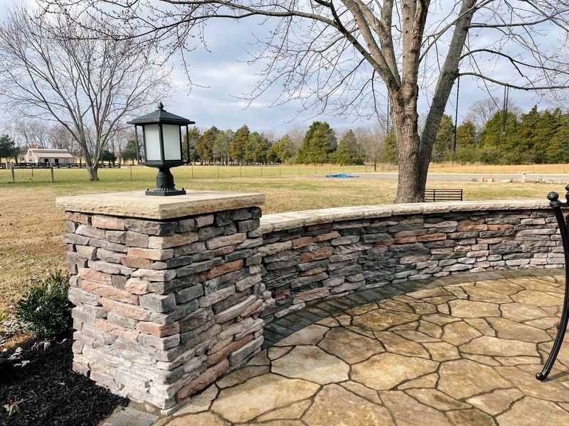 Stone wall with a light fixture and flagstone patio in a rural setting.