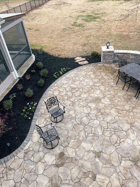 Overhead view of a stone patio with seating and landscaping around it next to a house.