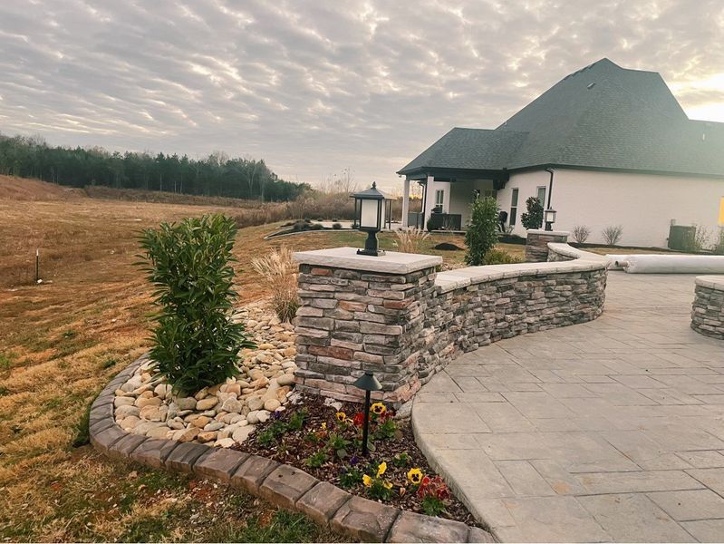 Stone pillars, patio, and landscaping in front of a house on a cloudy day.