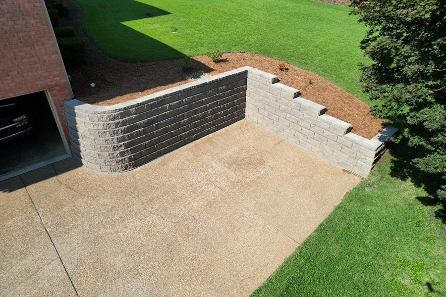 A concrete patio with retaining walls, built next to a garage and grassy hill.