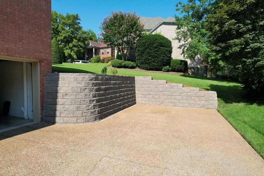Stone retaining wall next to a concrete driveway, separating a sloped lawn. Garage to the left.