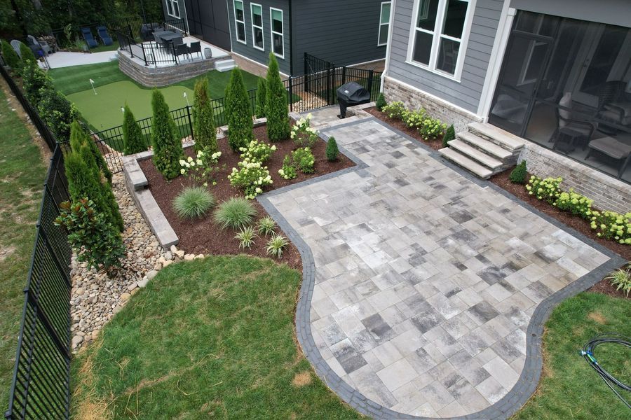 Backyard patio with gray pavers, landscaping, putting green, and a grill.