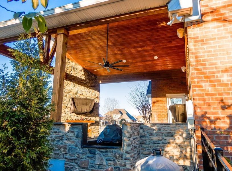 Covered outdoor patio with brick and stone, with a view of a backyard.