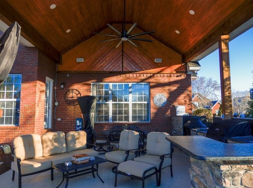 Covered patio with brick walls, seating, bar, and ceiling fan under a wood-paneled roof.