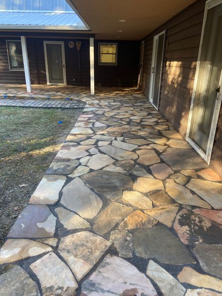 Stone pathway along a brown building with glass doors. Overhang and grassy area to the left.