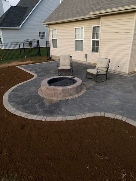 A patio with a fire pit and chairs. The backyard has a beige house and dark border.