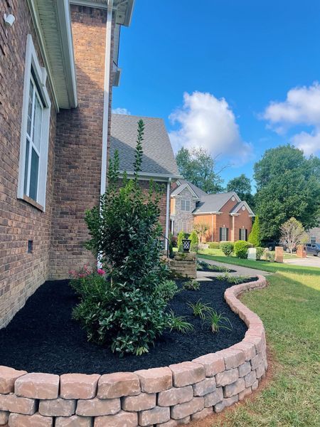 Brick home exterior with a landscaped flower bed and a curved retaining wall.