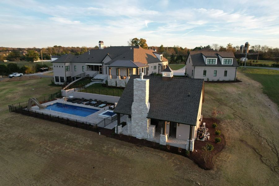 Aerial view of a large house with a pool, a guest house, and a farm setting on a sunny day.