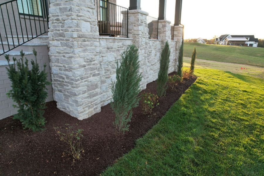 Stone house with small evergreen trees and a grassy lawn.