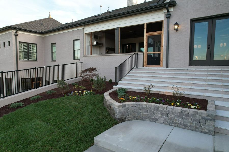 Exterior of a house with steps, landscaping, and a covered porch. Green grass and flower beds.