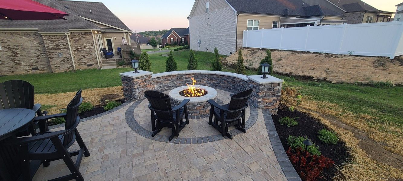 Backyard patio with a fire pit, two black chairs, and surrounding stone wall.