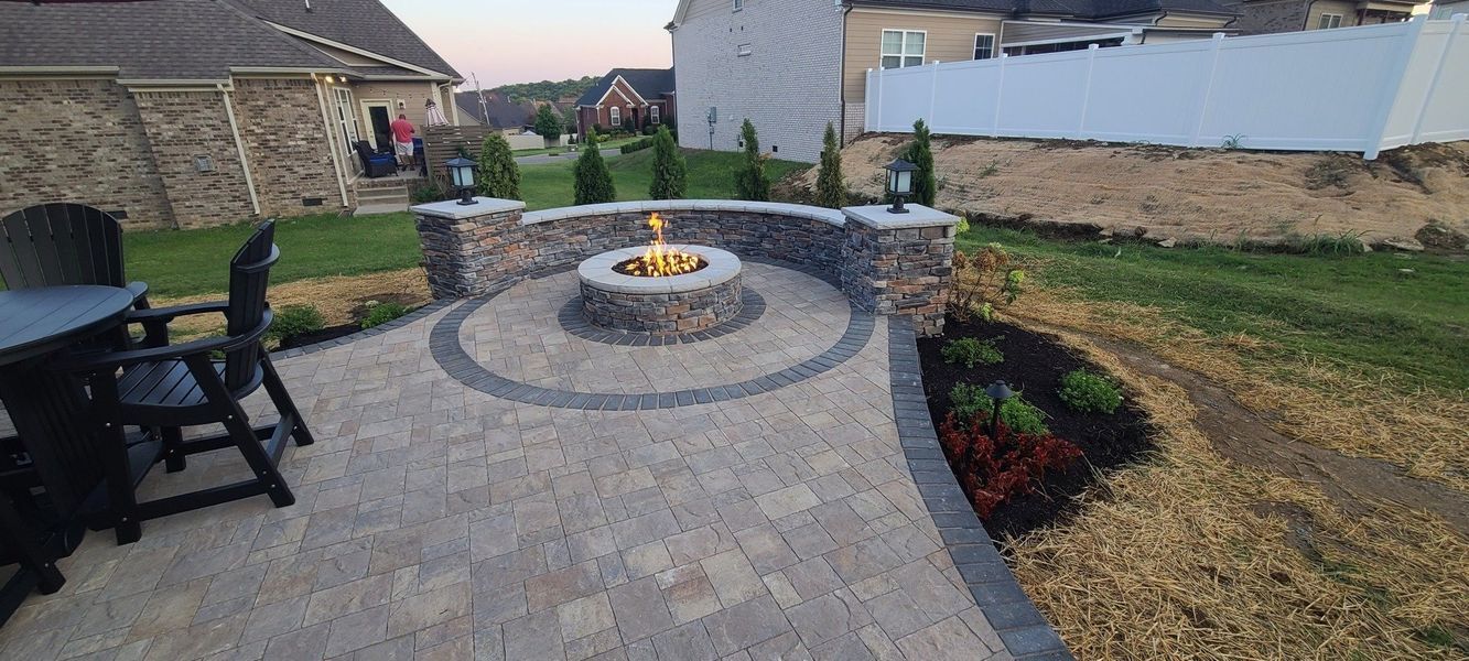 A backyard patio with a stone fire pit, seating, and landscaping.