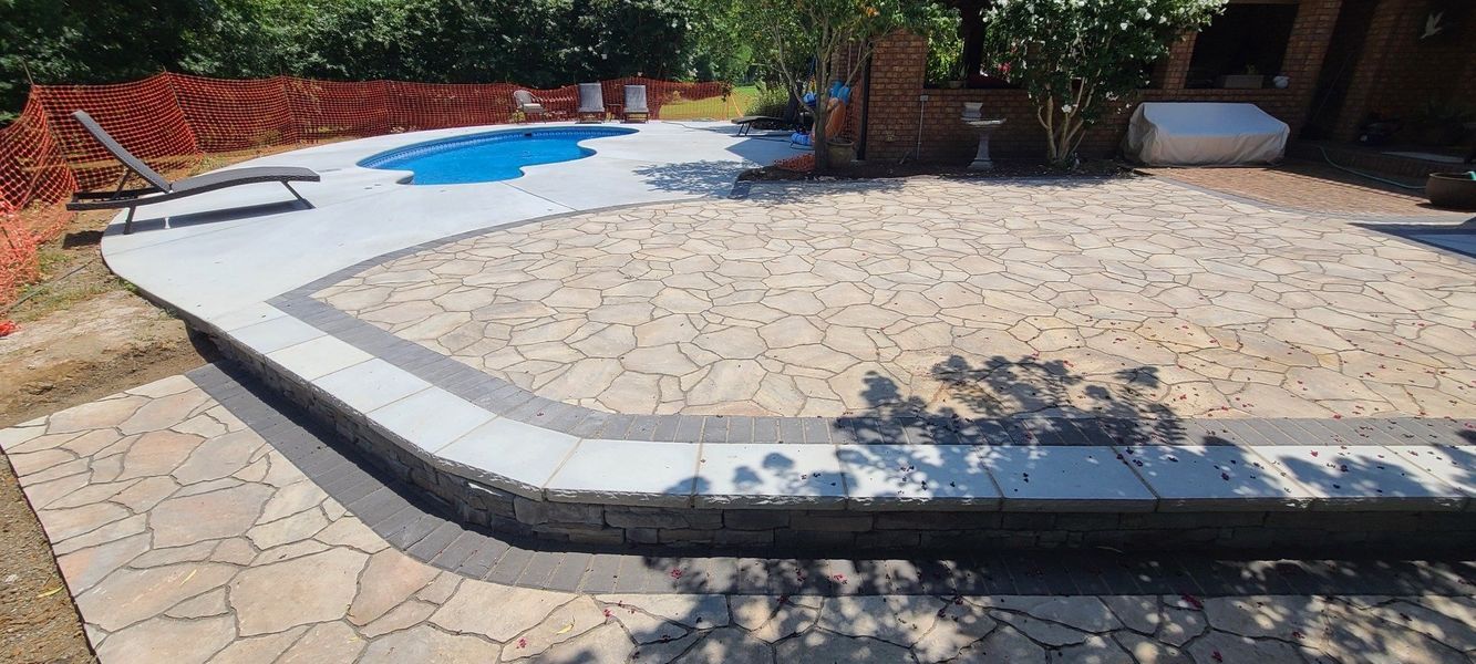 A pool area with stone patio, a blue pool, lounge chairs, and lush greenery.