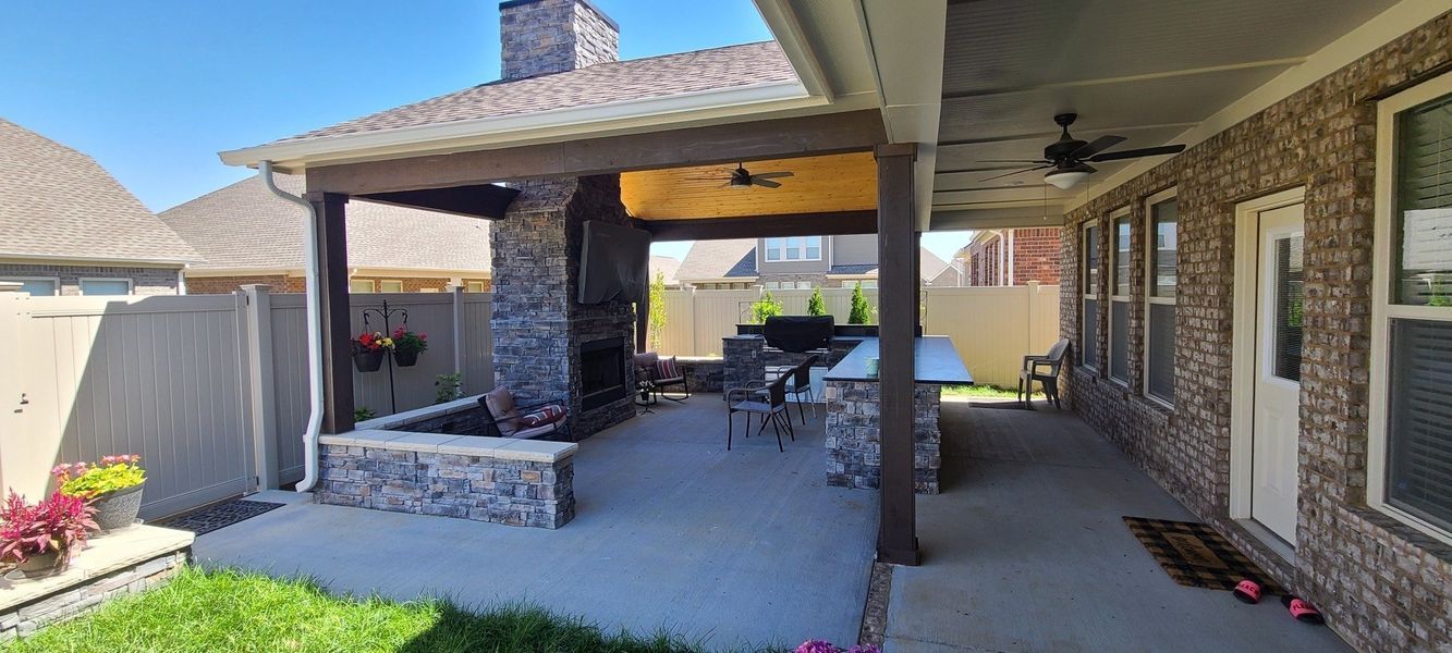 Outdoor patio with fireplace, grill, seating, and brown brick house exterior.