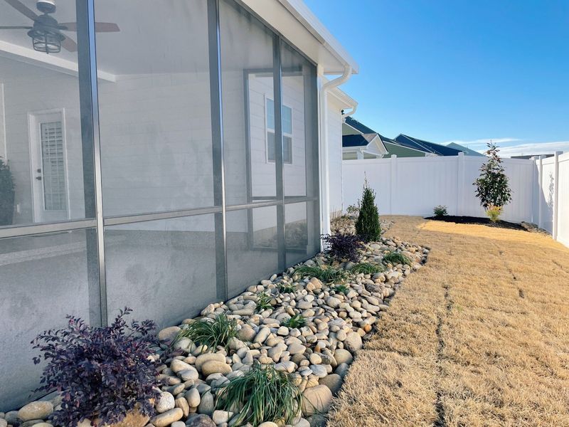 Backyard with screen enclosure, rock garden, white fence, and sunny blue sky.