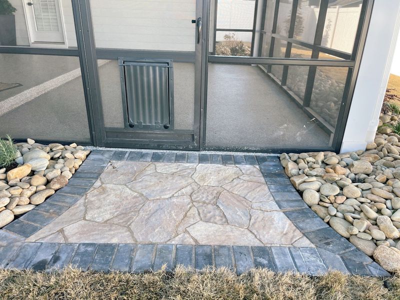A stone patio with a gray border in front of a screened-in porch with a pet door.