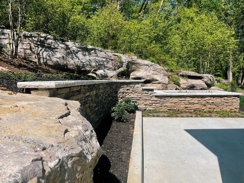 Stone walls and concrete patio with a rocky hillside and greenery in the background.
