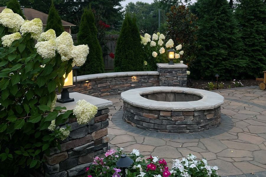 Stone patio with a fire pit, pillars with lights, and hydrangeas.