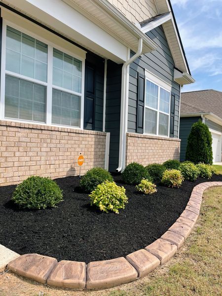 A house with a brick facade and dark siding. Landscaping with dark mulch, plants, and a decorative border.