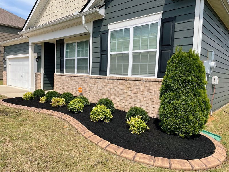 A house with a brick facade and dark blue siding. A landscaped bed of shrubs is in front.