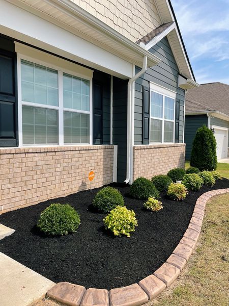 A house with a brick foundation and a landscaped bed of bushes bordered with brick.