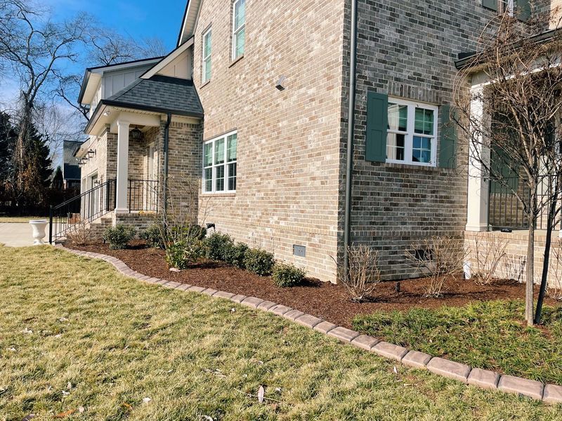 Brick house corner with landscaping. Green shutters, brown mulch, and lawn.