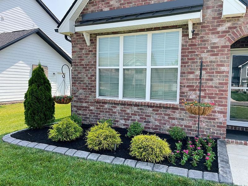 Brick home exterior with manicured landscaping, including a window, plants, and a black-mulched flowerbed.