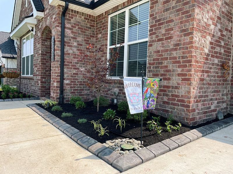 Brick house exterior with a freshly mulched flowerbed bordered by gray paving stones.