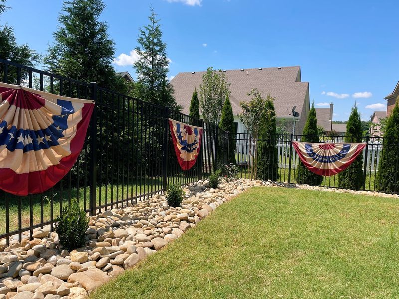 Backyard with patriotic bunting on black fence, green grass, and rock border.