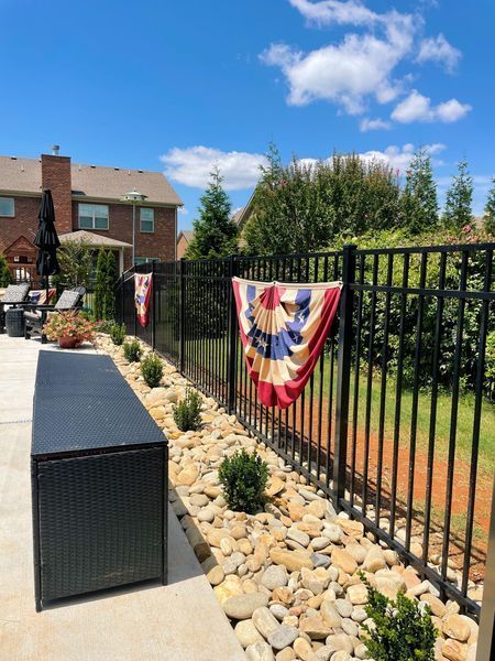 Backyard with a black fence decorated with red, white, and blue bunting, blue sky.