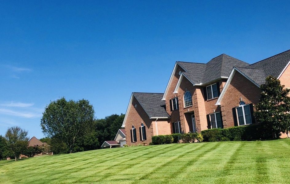 Brick house on a hill with freshly mowed lawn under a blue sky.