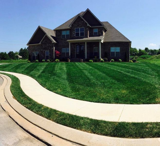Two-story brick house with striped green lawn and curving concrete sidewalk.