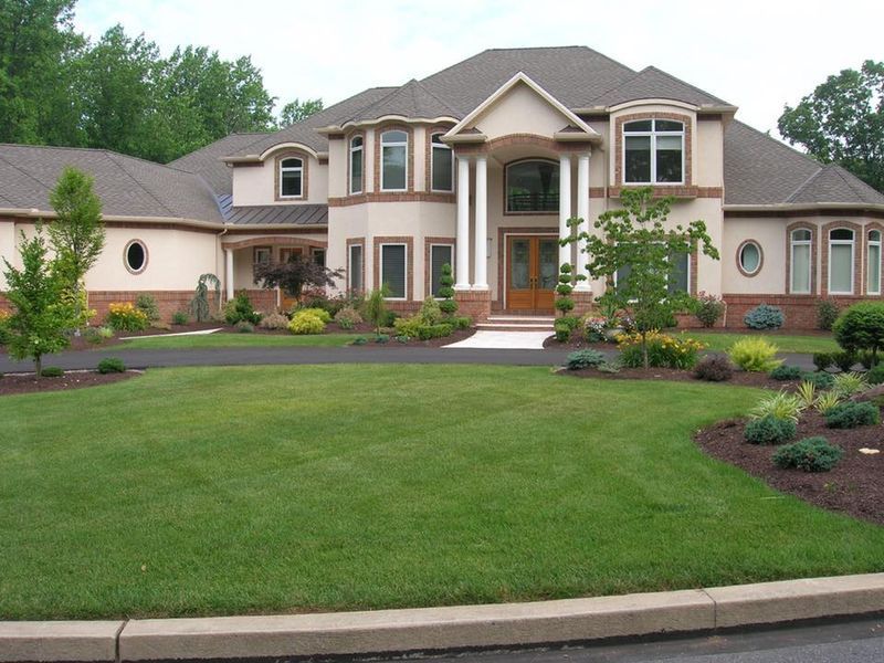 Large beige and tan house with a well-manicured lawn, trees, and landscaping.
